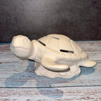 White ceramic turtle-shaped money box on a wooden surface with a gray background