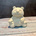 Unpainted ceramic bear figurine on a wooden surface with a neutral background