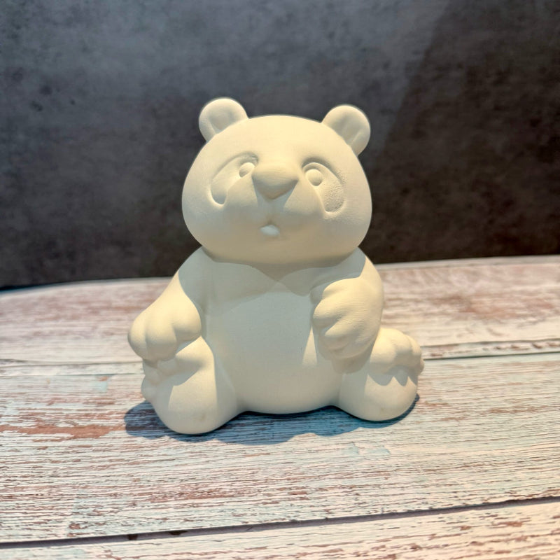 Unpainted ceramic bear figurine on a wooden surface with a neutral background