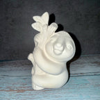 White ceramic sloth figurine with a leaf on a wooden surface