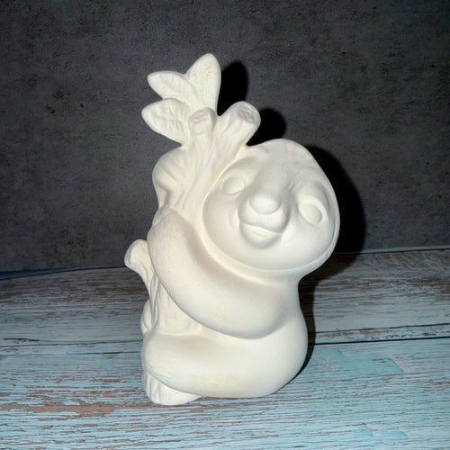 White ceramic sloth figurine with a leaf on a wooden surface