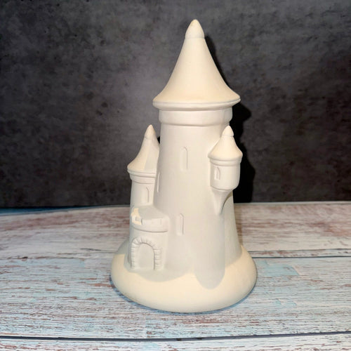 Unpainted ceramic castle on a wooden surface with a dark background