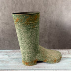 Green vintage-style rubber boot with rust spots on a wooden surface and gray background