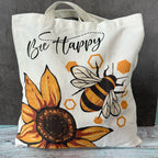 Tote bag with bee and sunflower design and 'Bee Happy' text on a gray background