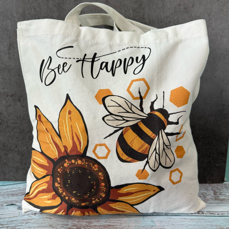 Tote bag with bee and sunflower design and 'Bee Happy' text on a gray background