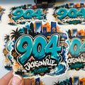 Sticker with '904 Jacksonville Florida' design held by a hand, with multiple stickers in the background.