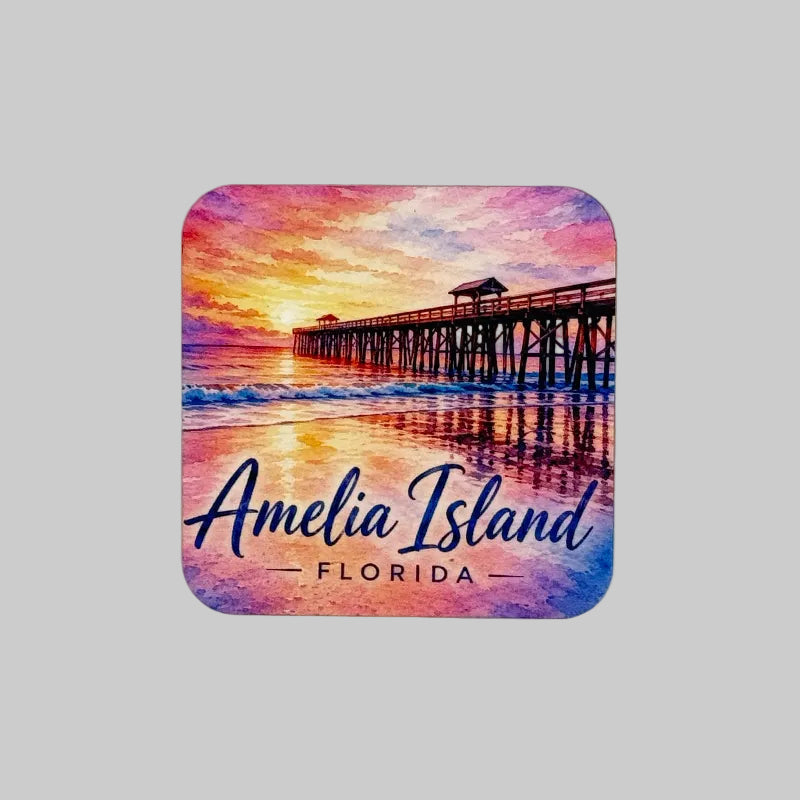 A square magnet with rounded corners featuring a colorful watercolor-style illustration of an Amelia Island, Florida sunset scene with a pier extending over the ocean. The text 'Amelia Island FLORIDA' is printed across the bottom in blue script and serif fonts.