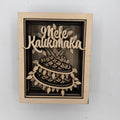 A square wooden wall art piece featuring a laser-cut 3D papercalix design of a kaliko fish with the words 'Mele Kaliko' in raised script above it, mounted on a light wood frame against a plain white wall.