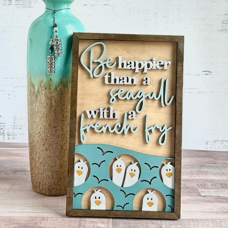 A wooden plaque with a laser cut design featuring a seagull and French fries, with a blue background and text.