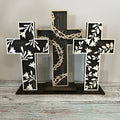 A layered cross decoration featuring three crosses arranged vertically with a floral and barbed wire design, predominantly in black and white, placed on a wooden surface.