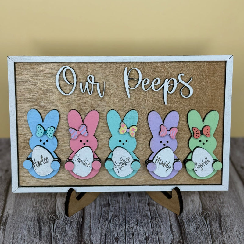 A 3D layered decorative sign with colorful bunny shapes and the text 'Our Peeps' on a wooden surface.