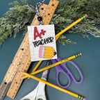 School supplies including pencils, scissors, and a ruler on a dark surface with a 'A+ Teacher' card.