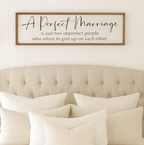A Perfect Marriage wedding sign for above you master bedroom. Neatly made bed with decorative pillows and a framed quote above it in a bedroom setting.