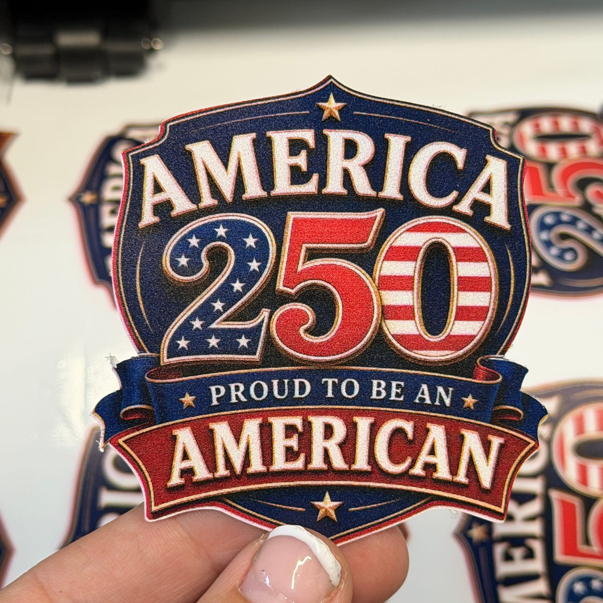 Sticker with 'America 250 Proud to be an American' design held by a hand.