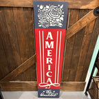 Decorative sign with floral design and 'America the Beautiful' text against a wooden background