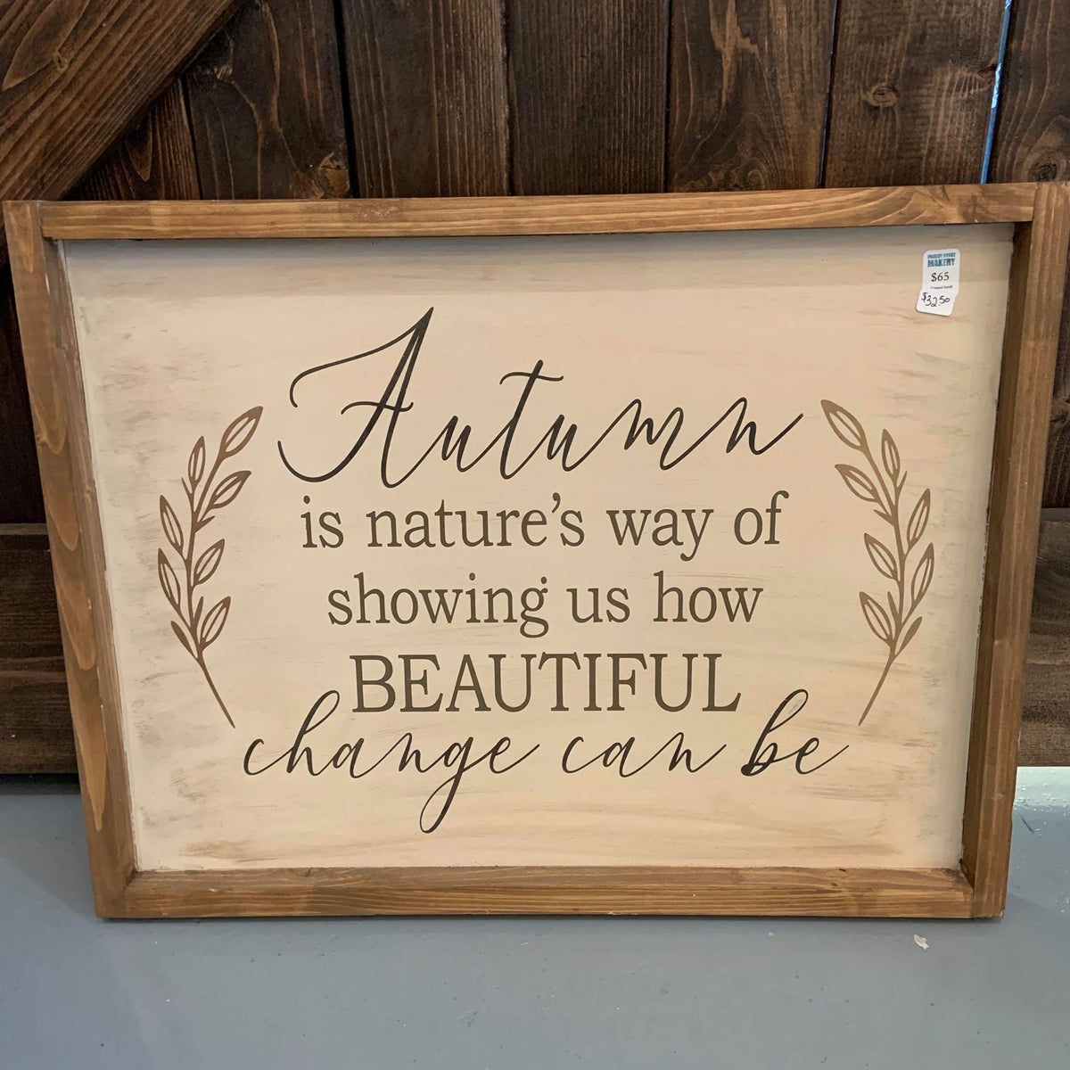 A seasonal decor sign that reads 'Autumn is nature's way of showing us how beautiful change can be', with a leaf pattern around the text, framed in a wooden border.