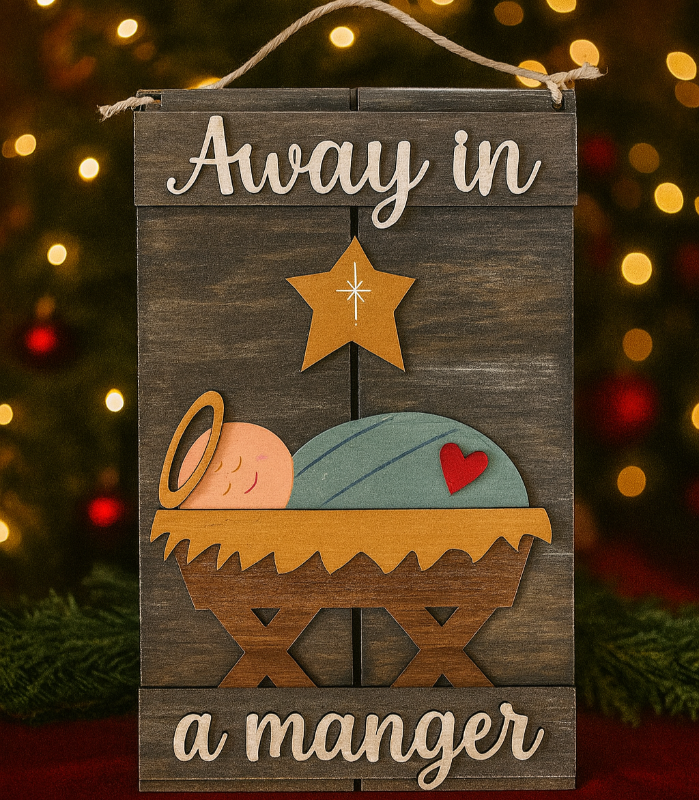 Decorative sign with nativity scene and 'Away in a manger' text against a Christmas tree background.