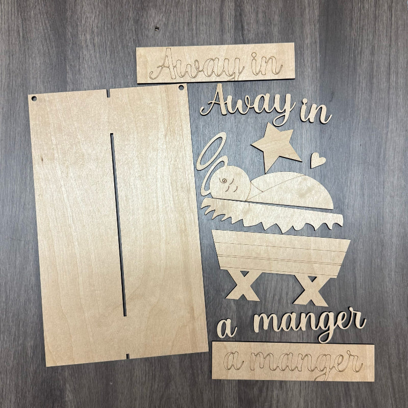 Wooden nativity scene cutout with 'Away in a manger' text on a wooden background