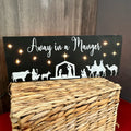 A nativity scene lighted sign featuring a manger with livestock around it, and the text 'Away in a Manger' at the top.
