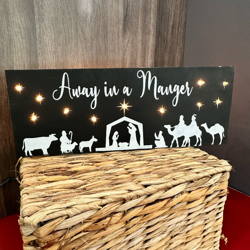 A nativity scene lighted sign featuring a manger with livestock around it, and the text 'Away in a Manger' at the top.