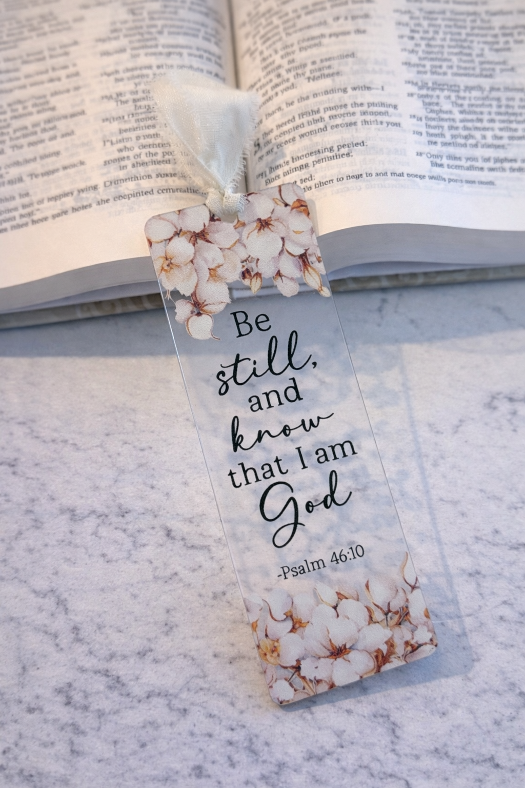 Floral bookmark with 'Be still and know that I am God' text on a marble surface