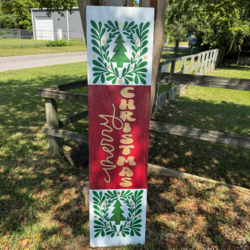 Christmas-themed decorative sign with wreaths and 'Merry Christmas' text on a wooden post outdoors.