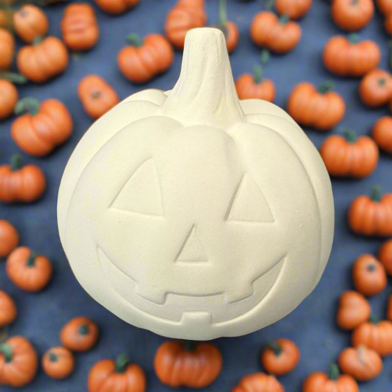 Unpainted ceramic pumpkin with jack-o'-lantern face on a wooden surface