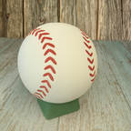 Baseball with red stitching on a green stand against a wooden background