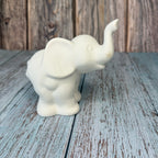 White ceramic elephant figurine on a wooden surface with a rustic background