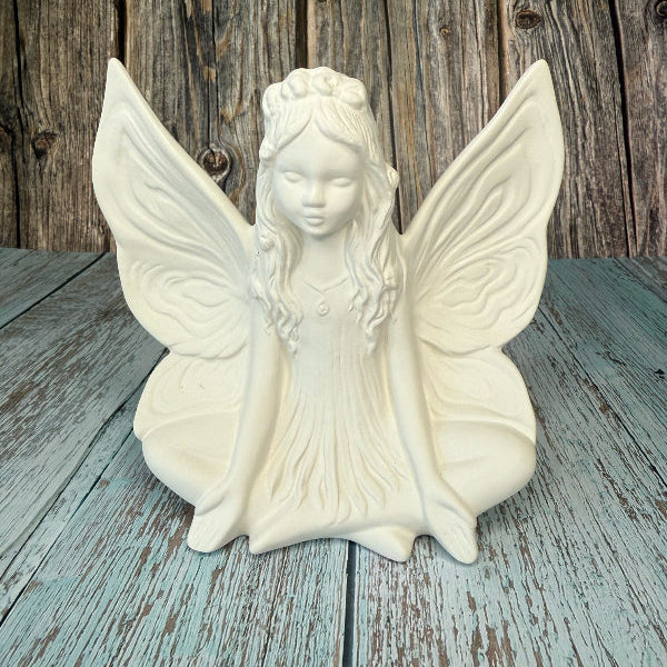 White ceramic fairy figurine with butterfly wings on a wooden surface