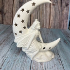 Decorative statue of a woman on a crescent moon with star details, placed on a wooden surface.