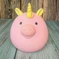 Pink piggy bank with yellow unicorn horns on a wooden surface