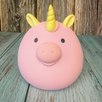 Pink piggy bank with yellow unicorn horns on a wooden surface