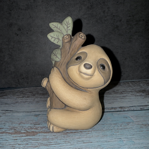 Ceramic sloth figurine with a branch and leaf on a wooden surface