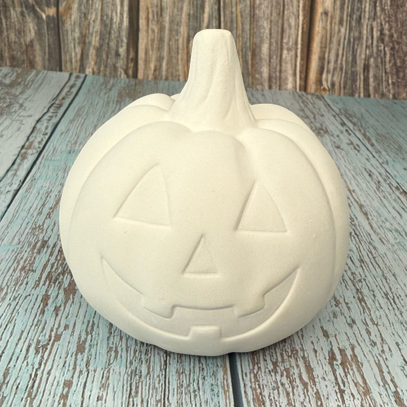 Unpainted ceramic pumpkin with jack-o'-lantern face on a wooden surface