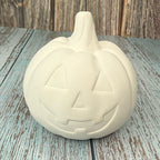 Unpainted ceramic pumpkin with jack-o'-lantern face on a wooden surface
