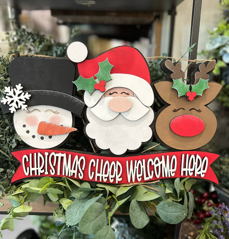 Decorative Christmas sign with Santa, reindeer, and snowman on a green wreath.