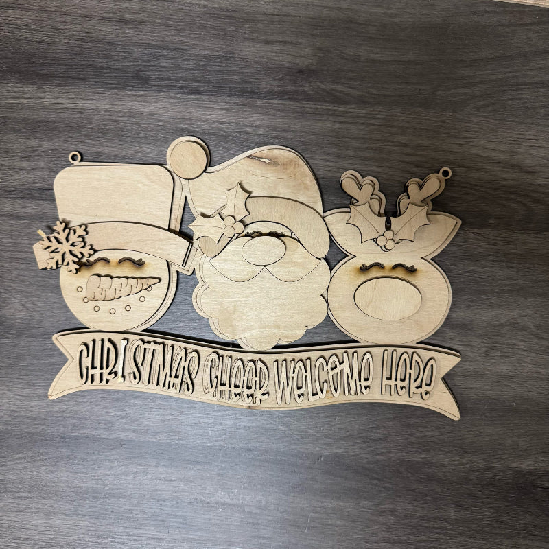 Wooden Christmas decoration with Santa Claus face and 'Christmas Gilded Welcome Here' banner on a wooden background