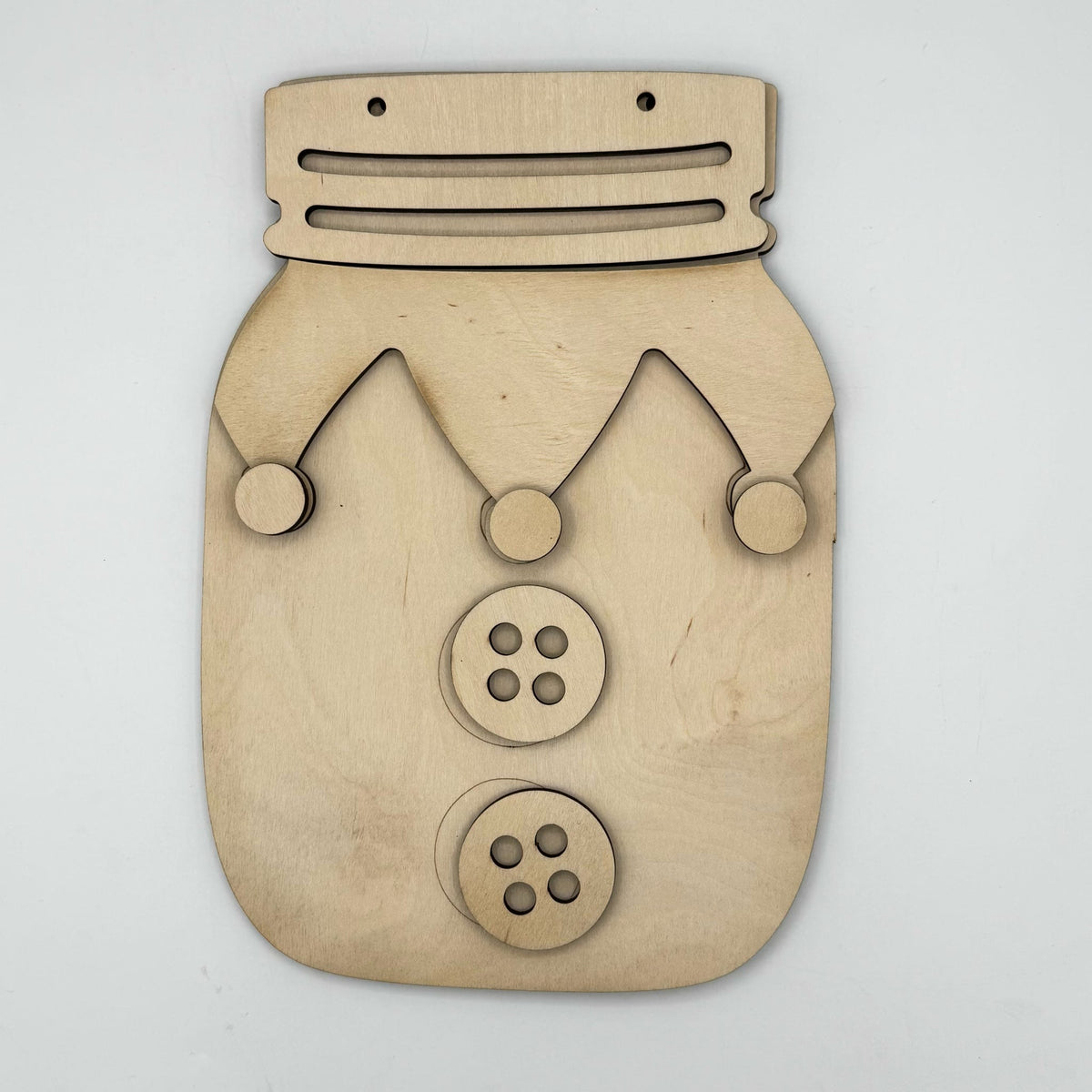 A laser-cut wooden jester mask or decorative plaque shaped like a mason jar, made from light natural wood with cutout facial features and two button details, shown on a plain light background.