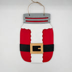 A Santa Claus-themed mason jar hanging ornament made from painted wood, featuring red body sections, a white vertical section, a black belt, a tan buckle, and a gray top with twine hanger.