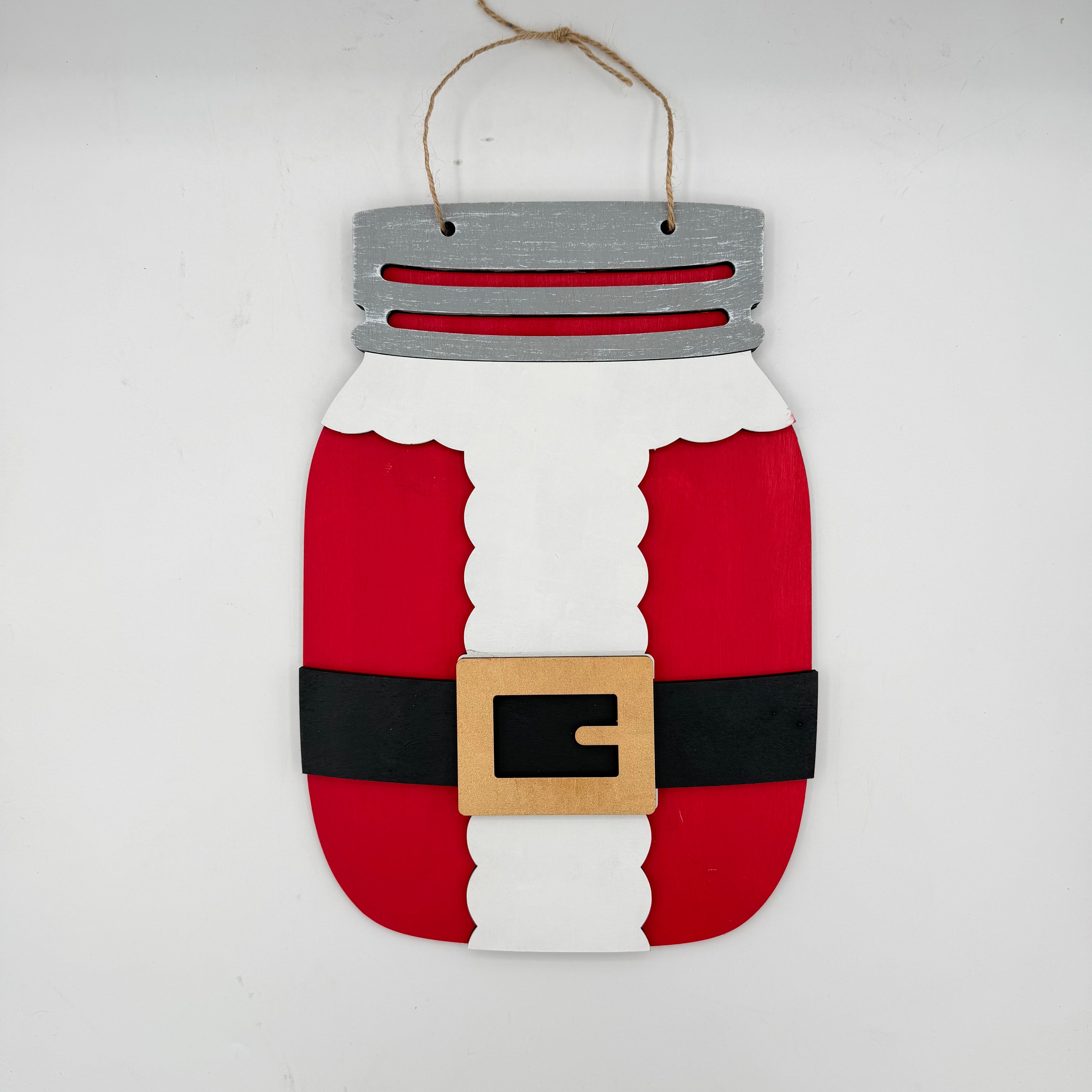 A Santa Claus-themed mason jar hanging ornament made from painted wood, featuring red body sections, a white vertical section, a black belt, a tan buckle, and a gray top with twine hanger.