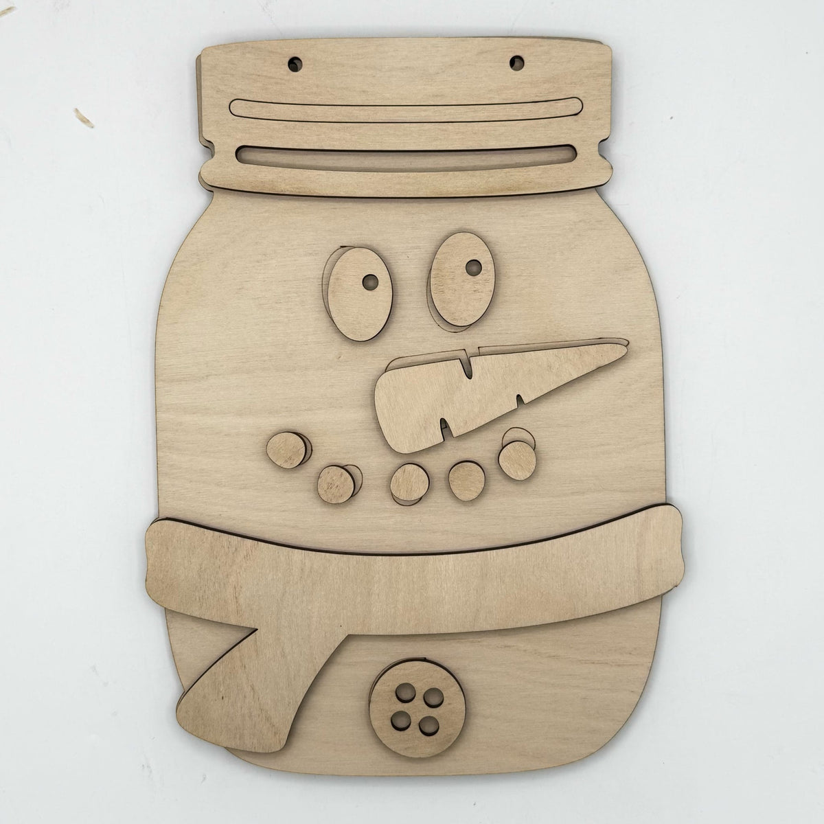 A wooden snowman face cutout or wall decor piece made from light natural wood, featuring cutout eyes, nose, buttons, and a hat, shown on a plain white background.