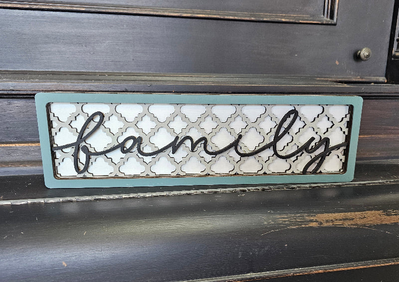 A rectangular chunky shelf sitter with a gray background and the word 'Family' in a cursive script on the front, placed on a wooden surface.