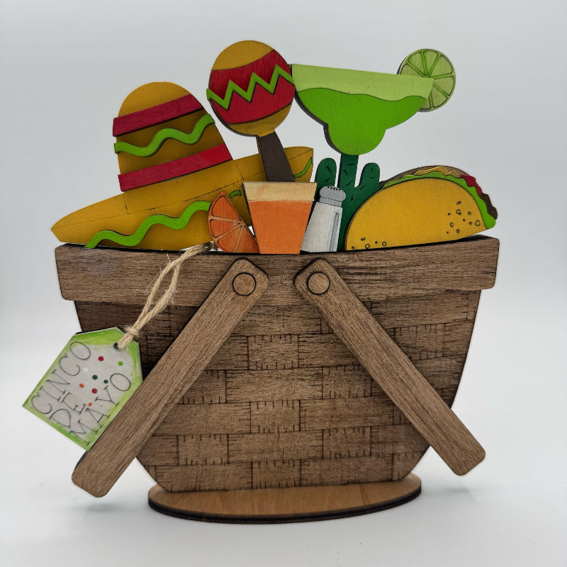 Decorative basket with Mexican-themed items including a sombrero, tacos, and a bottle, on a white background.
