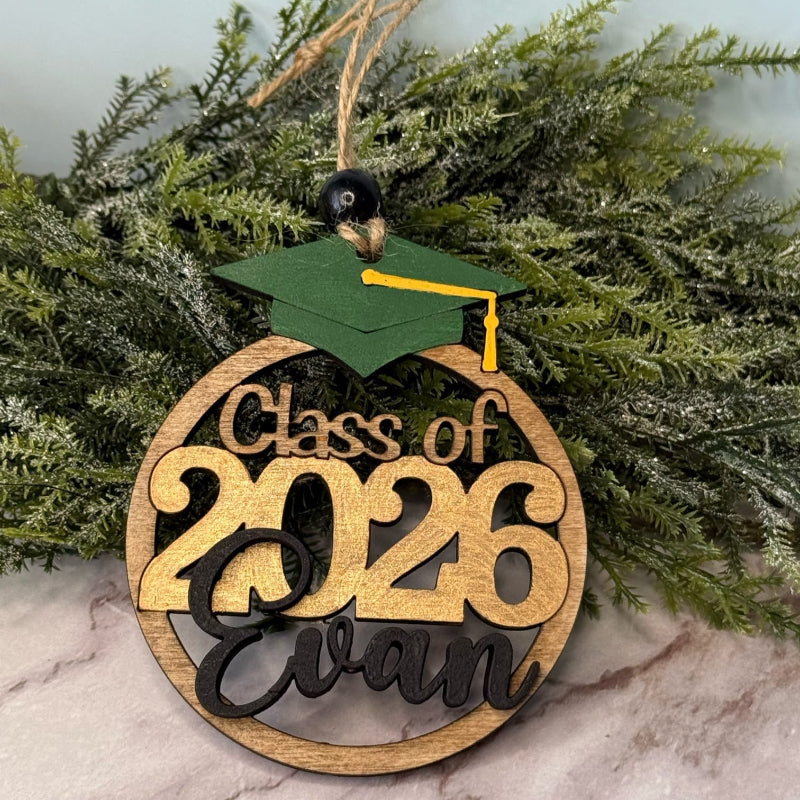 Graduation-themed wooden ornament with 'Class of 2026' and name 'Evan' on a greenery background