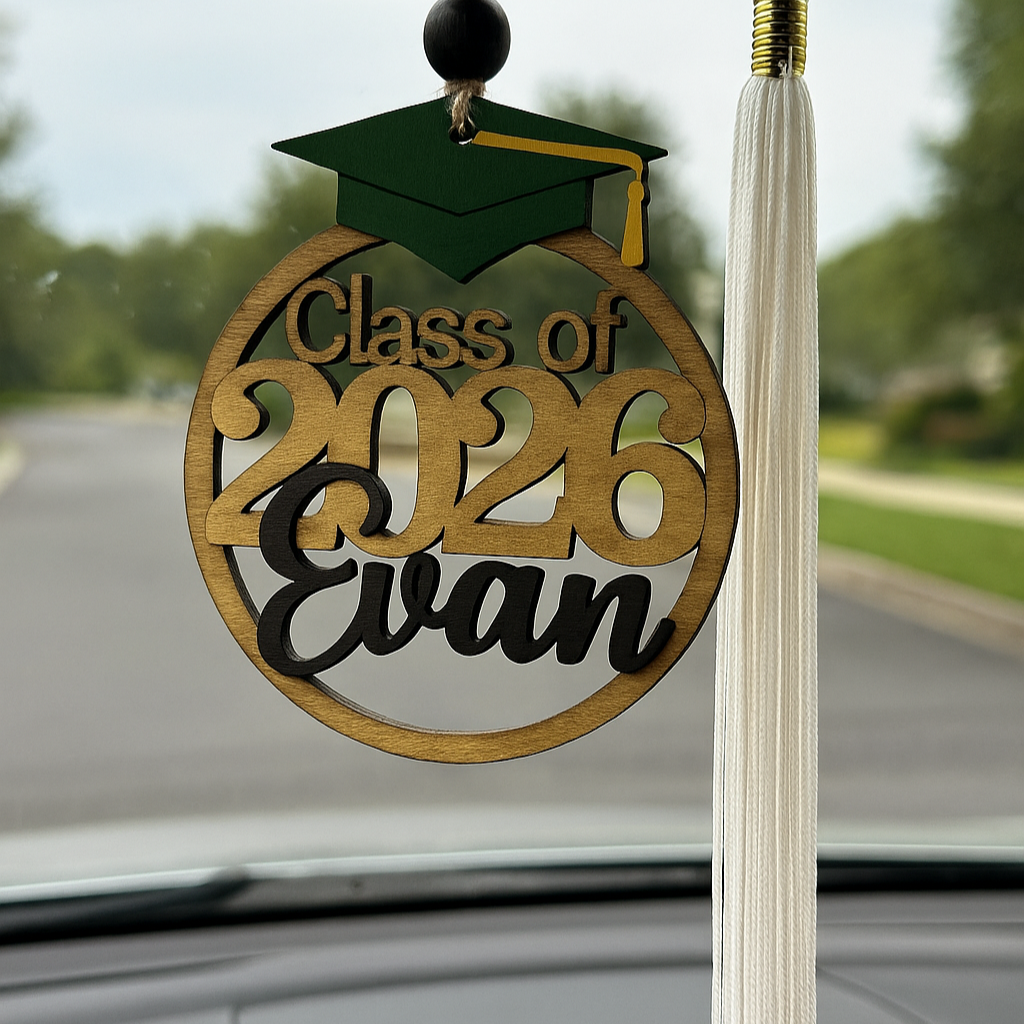 Graduation-themed car ornament with 'Class of 2026 Evan' text hanging from a car's rearview mirror.