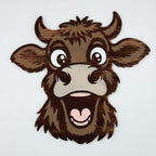 A cartoon-style wooden cow head sign with dark brown and medium brown wood grain, white eyes, and a pink heart-shaped mouth, shown against a plain light gray background.