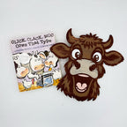 A cartoon cow head cutout or sticker placed next to a small children's book titled "Click, Clack, Moo Cows That Type" on a plain white background.