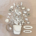 A flat-lay arrangement of light-colored wooden beach-themed cutouts and shapes, including a bucket, starfish, seahorse, crabs, shells, sand dollars, a shovel, and two oval pieces, laid on a tan background.