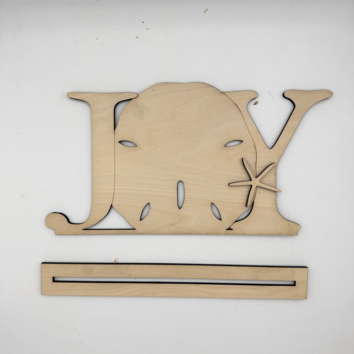 A natural wood decorative sign shaped like the word 'JOY' with a starfish detail, shown above a matching wooden mounting strip on a plain white background.